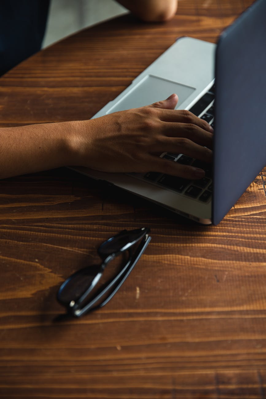 crop faceless person browsing laptop at round table