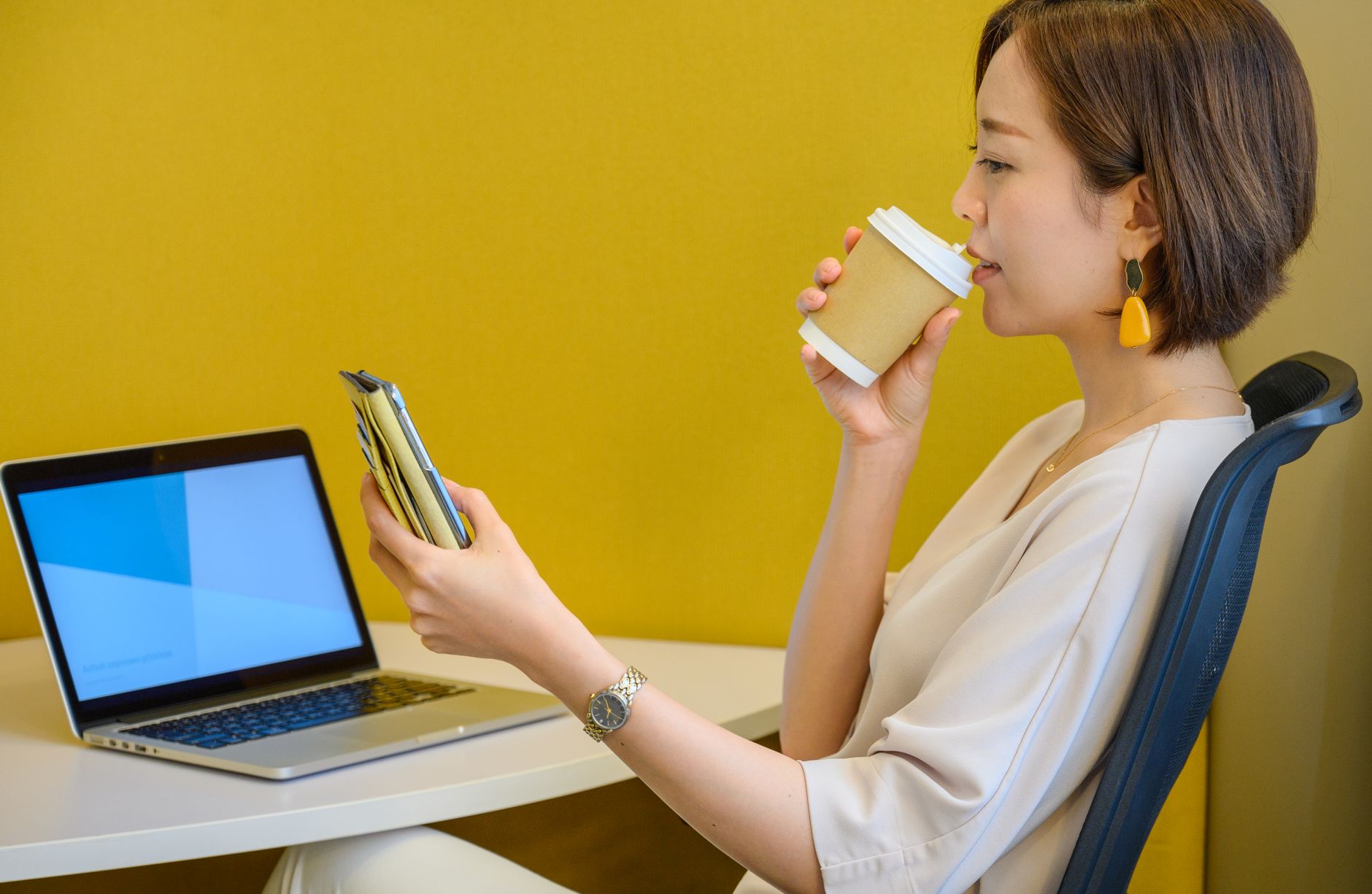woman drinking on a paper cup with lid while looking at her smartphone
